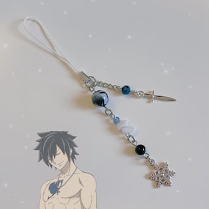 Może przedstawiać: Srebrny charm z płatkiem śniegu, mieczem i koralikami. Charm jest przymocowany do białego sznurka.