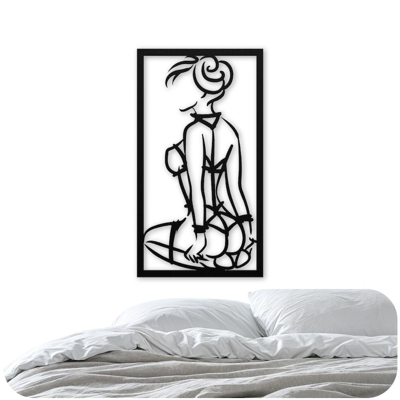 Puede incluir: Decoraci&oacute;n de pared de arte de l&iacute;nea en blanco y negro con una mujer en lencer&iacute;a. La mujer se representa en una pose de rodillas con la espalda al espectador. La obra de arte est&aacute; enmarcada en un rect&aacute;ngulo negro.