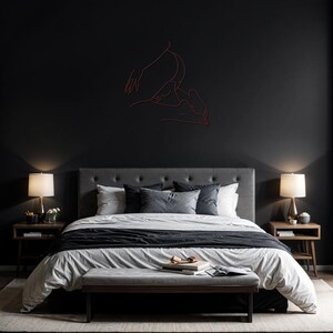 May include: A black and white bedroom with a gray headboard and a white duvet cover. The bed has a black throw blanket and a gray bench at the foot of the bed. There are two bedside tables with lamps and a line drawing of two figures on the wall.