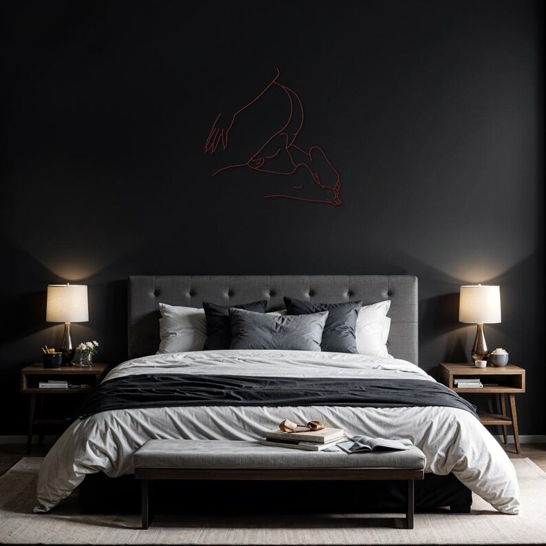 May include: A black and white bedroom with a gray headboard and a white duvet cover. The bed has a black throw blanket and a gray bench at the foot of the bed. There are two bedside tables with lamps and a line drawing of two figures on the wall.