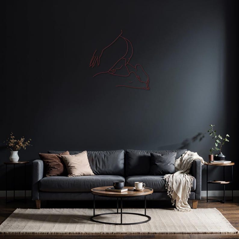 May include: A dark gray sofa with two brown pillows and a white throw blanket. The sofa is in front of a dark gray wall with a red line drawing of two figures.