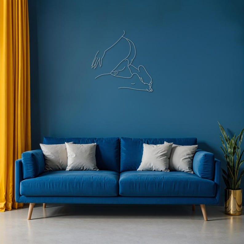 May include: A blue velvet sofa with three white throw pillows in front of a blue wall with a white line drawing of a person.