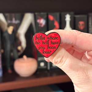Op de afbeelding: Rode hartvormige emaille pin met zwarte tekst "Bella, where the hell have you been loca?"