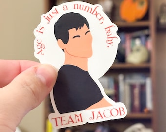 Op de afbeelding: Een witte sticker met een gestileerde illustratie van een persoon met zwart haar en een zwart shirt. De sticker heeft de tekst "Age is just a number, baby." en "TEAM JACOB" in het rood.