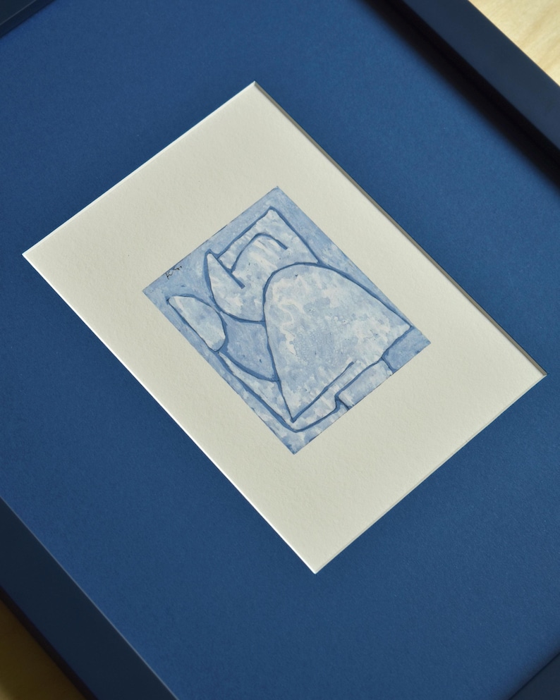 May include: Abstract blue ink drawing in a white mat, set in a dark blue frame. The artwork features a minimalist design with geometric shapes and lines. The frame is a deep navy blue, creating a striking contrast with the artwork.