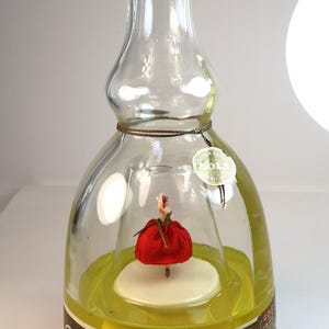 Peut inclure: Bouteille vintage Bols Ballerina avec un bouchon rouge. À l'intérieur, une ballerine miniature en robe rouge se tient sur une plateforme blanche. La bouteille a une étiquette marron avec des lettres dorées et un liquide jaune.