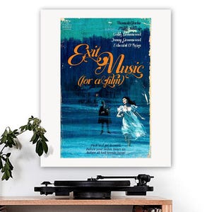 Puede incluir: Una impresión artística enmarcada titulada "Exit Music (for a film)" con un diseño de cartel de película vintage. La obra de arte presenta un fondo azul oscuro y verde azulado con texto naranja y una escena de dos figuras. La impresión se muestra sobre una superficie de madera.