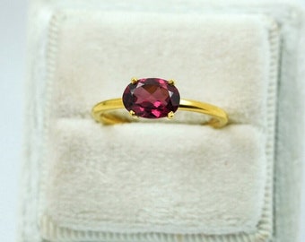 May include: A gold ring with a deep red oval gemstone set in the center.