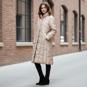 May include: A long, beige quilted coat with a high collar and button closure. The coat features a diamond pattern and pockets. The person is wearing black pants and black ankle boots. The background includes a brick building and windows.
