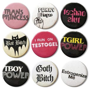 Könnte beinhalten: Eine Sammlung von neun runden Ansteckbuttons mit verschiedenen Phrasen und Grafiken. Die Buttons zeigen Texte wie "TRANS PRINCESS", "FUNKY Finger" und "techno slut". Die Farben sind Rosa, Schwarz, Weiß und Rot. Die Buttons sind wahrscheinlich als Neuheiten oder Accessoires gedacht.