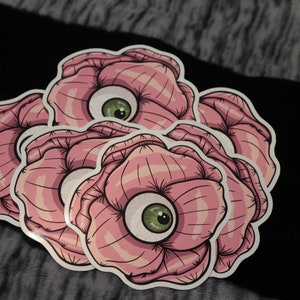 May include: Three pink flower stickers with green eyes in the center of each flower. The flowers have a striped pattern.