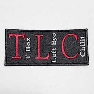 Könnte beinhalten: Schwarzer rechteckiger Aufnäher mit rotem gesticktem Text. Der Text lautet "TLC" mit den Namen "T-Boz", "Left Eye" und "Chilli" vertikal ausgerichtet. Der Aufnäher befindet sich auf einer weißen Oberfläche.
