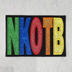 May include: A rectangular black patch featuring the glittery, multi-colored letters NKOTB. The N is green, the K is blue, the O is red, the T is orange, and the B is yellow. Each letter is outlined in a matching thread color on a black background.