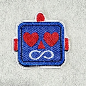 以下が含まれることがあります： 青いロボットの頭部が刺繍された四角いワッペン。赤いハート型の目、小さな赤い三角形の鼻、白い無限大記号の口が特徴。ワッペンの上部には小さな赤いアンテナがあり、両サイドにも赤い突起が付いている。