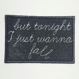 May include: A rectangular black patch with white embroidered text. The text reads "but tonight I just wanna fall" in a cursive font. The patch has a dark gray border.