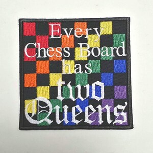 May include: Square patch with a black border and a rainbow checkerboard pattern. White text reads "Every Chess Board has two Queens". The patch is embroidered with a variety of colors, including red, orange, yellow, green, blue, and purple.