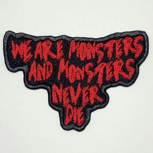 May include: Embroidered patch with the text "WE ARE MONSTERS AND MONSTERS NEVER DIE" in red on a black background. The patch has a black border and is likely designed to be sewn or ironed onto fabric.