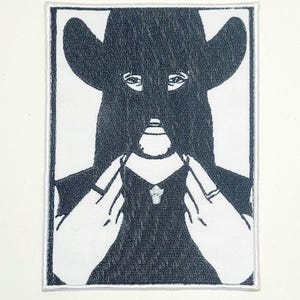May include: A black and white patch featuring a figure wearing a hat and a mask, with hands holding the collar of a garment. The design is a stylized illustration with a textured appearance, set against a white background.
