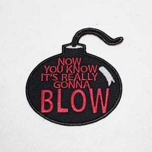 May include: Black embroidered patch in the shape of a bomb with the text "NOW YOU KNOW IT'S REALLY GONNA BLOW" in red. The patch has a black outline and a curved black fuse.
