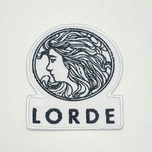 May include: White embroidered patch featuring a black and white illustration of a woman's profile within a circle. The word "LORDE" is embroidered in black block letters below the circle.