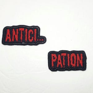 May include: Two black fabric patches with red embroidered text. The first patch says "ANTICl..." and the second patch says "PATlON".