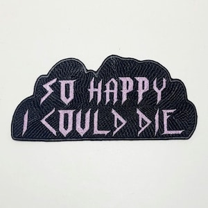 May include: A black embroidered patch in the shape of a cloud. The patch features the phrase "SO HAPPY I COULD DIE" in lavender-colored, gothic-style lettering. The patch is on a white background.