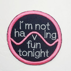 May include: A black and pink round embroidered patch with the text "I'm not having fun tonight" in white.