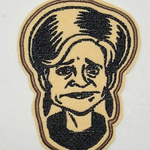 May include: A brown embroidered patch with a black and white image of a woman with a sad expression. The woman has short, wavy hair and is wearing a dark shirt.