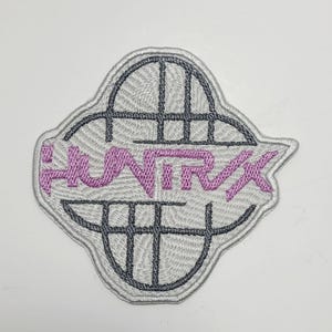 Peut inclure: Écusson brodé avec le mot "HUNT RX" en lavande, sur un fond gris avec un motif de grille noire. Le patch a une bordure grise et est destiné aux vêtements ou accessoires.