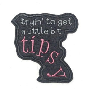 Puede incluir: Parche bordado negro con el texto "tryin' to get a little bit tips" en hilo blanco y rosa.