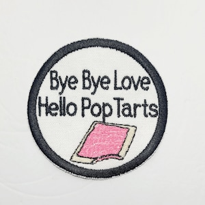 May include: A white round embroidered patch with a black border. The patch says "Bye Bye Love Hello Pop Tarts" with a pink and white Pop Tart illustration.