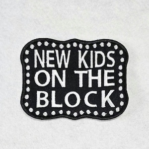 May include: A rectangular embroidered patch with scalloped edges featuring a black background and white border dots. The text NEW KIDS ON THE BLOCK is stitched in white capital letters across the center of the patch in a bold, sans-serif font.