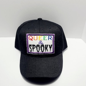 May include: Black baseball cap with a rainbow embroidered patch that says "QUEER & SPOOKY" in white letters.