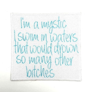 May include: Square white patch with embroidered text in light blue. The text reads: "I'm a mystic I swim in waters that would drown so many other bitches."