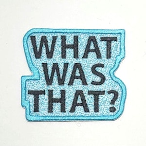 May include: A rectangular patch with the words "WHAT WAS THAT?" in black, embroidered on a light blue background. The patch has a textured appearance and a light blue border.