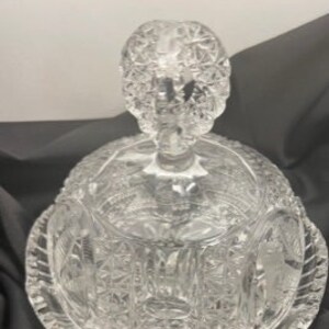 May include: A clear glass butter dish with a domed lid and a decorative handle. The dish has a cut glass pattern.