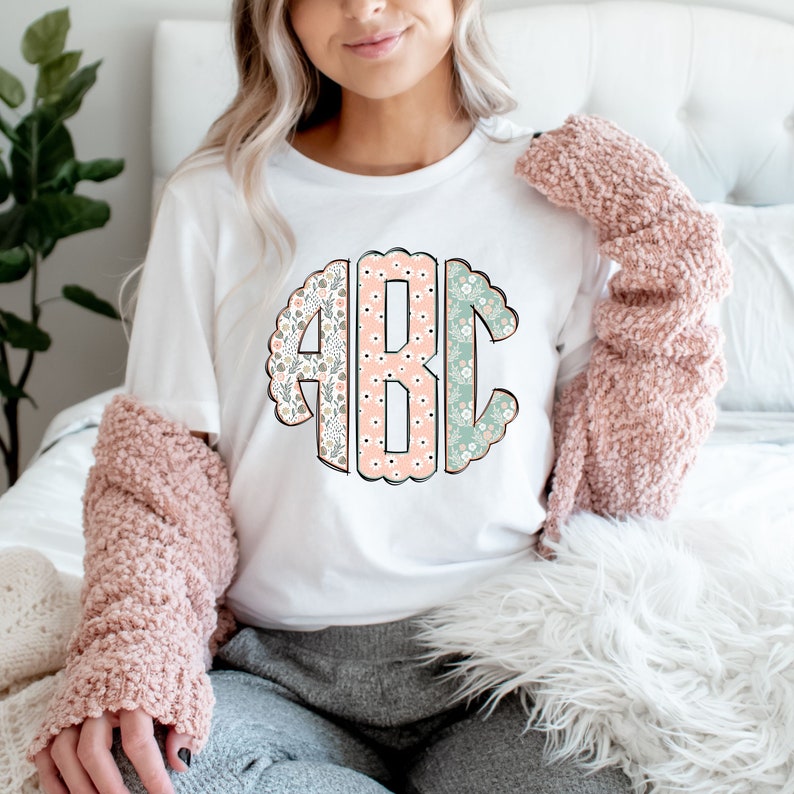 May include: White t-shirt with a floral monogram design featuring the letters "ABC" in a circle.
