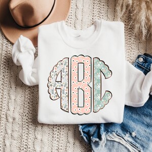 May include: White sweatshirt with a floral monogram design featuring the letters "ABC" in a circle.