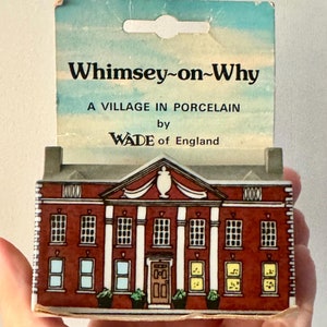 Puede incluir: Un edificio de ladrillo rojo con molduras blancas y una puerta blanca. El edificio tiene un letrero que dice "Whimsey-on-Why A VILLAGE IN PORCELAIN by WADE of England".