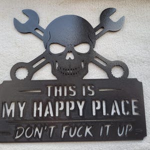 May include: A black metal wall sign featuring a skull centred above two crossed wrenches. Below the skull, a rectangular plaque displays the text "THIS IS MY HAPPY PLACE" in large letters, followed by the phrase "DON'T FUCK IT UP" in smaller text.
