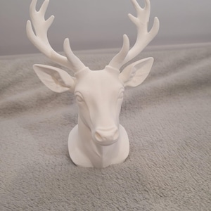 May include: A white deer head sculpture with detailed antlers and facial features. The sculpture is made of a solid material and is designed to be mounted on a wall. The deer head is a decorative item, suitable for home decor.