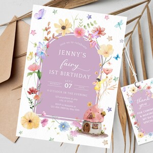 May include: A purple and white invitation with a watercolor illustration of a fairy house, flowers, and fairies. The text reads "Join us to celebrate Jenny's fairy 1st birthday, Monday, Sept 07, 4 o'clock in the evening, 123 anywhere stany, city, st 12345, RSVP to Natasha at 123-456-7890 by May 10th". A matching thank you tag with the text "Thank you for coming & making my day special" is also included.