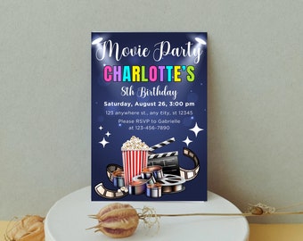 Może przedstawiać: Niebieskie zaproszenie na imprezę filmową z kolorowym tytułem: "Movie Party Charlotte's 8th Birthday". Zaproszenie zawiera grafikę popcornu, czerwono-białego pasiastych kubełków na popcorn i szpul filmowych.