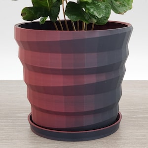 May include: A red and black geometric planter with a plant inside. The planter has a textured, ridged design.