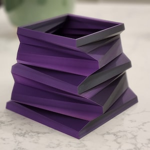 May include: A purple geometric planter made of stacked, angled squares. The planter has a modern, minimalist design.