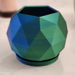 May include: A geometric planter with a blue and green gradient finish. The planter has a round base and a geometric top.