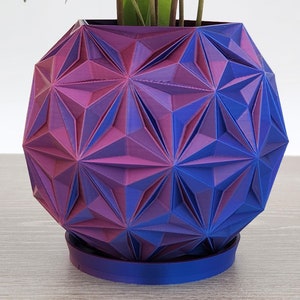 May include: A geometric purple and blue planter with a starburst pattern. The planter has a round base and is made of a smooth, glossy material.