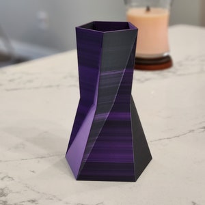 May include: A purple and black geometric vase with a hexagonal base and a unique, twisted design.