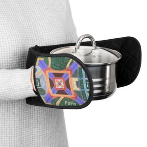 May include: Black oven mitts with a colorful geometric design and the word "Paris" printed on the front. The mitts are holding a stainless steel pot with a glass lid.