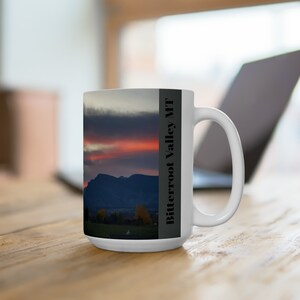 May include: White ceramic mug with a scenic image of a mountain range at sunset with a cloudy sky. The text "Bitterroot Valley MT" is printed on the side of the mug.